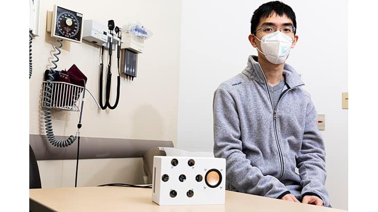 Lead author Anran Wang, a UW doctoral student in the Paul G. Allen School of Computer Science & Engineering, sits with the smart speaker prototype (white box in foreground) the team used for the study.