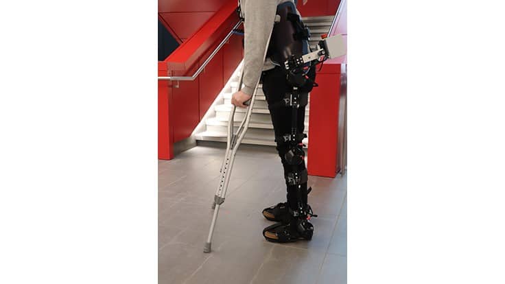 Someone using an exoskeleton leg capable of thinking and moving on its own using sophisticated artificial intelligence technology approaches stairs.