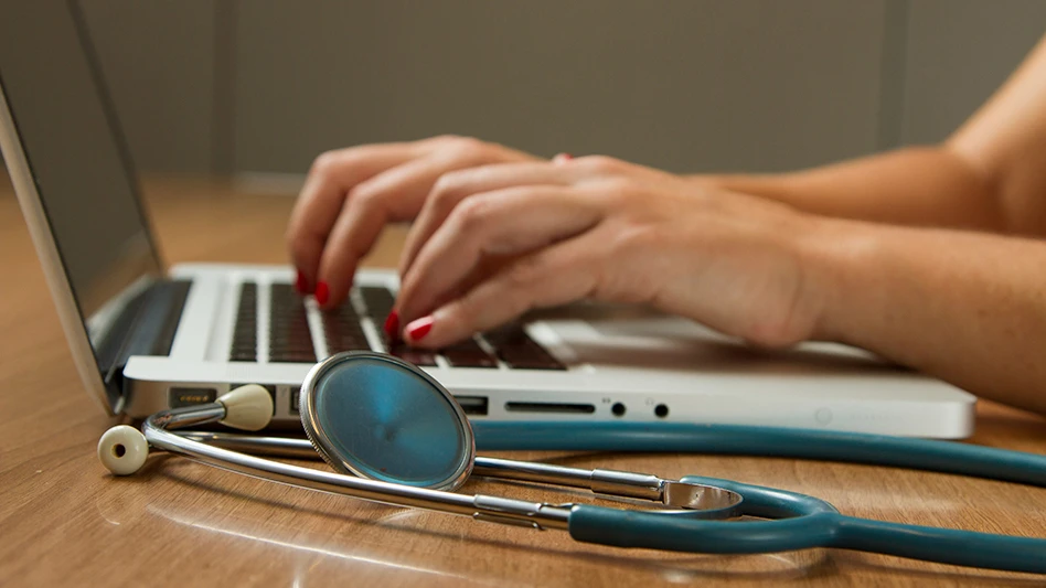 Hands typing on a laptop next to a stethoscope